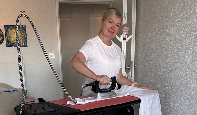 Person, die einen Edelstahlofen mit gelben Handschuhen, einem grünen Tuch und einer roten Sprühflasche reinigt.