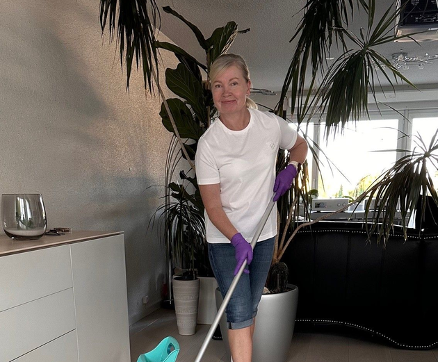 Eine blaue Scheuerbürste mit gelben Borsten fegt Seifenwasser über eine nasse, graue Oberfläche.