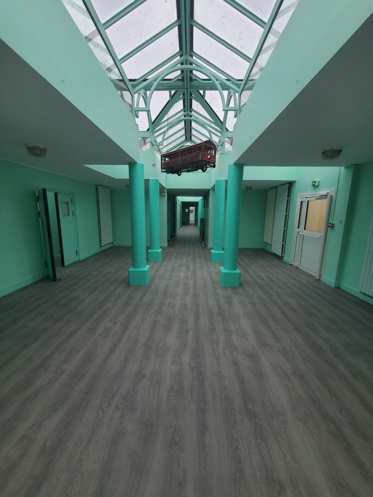 Couloir turquoise vide avec des portes des deux côtés et un plafond éclairé par une verrière