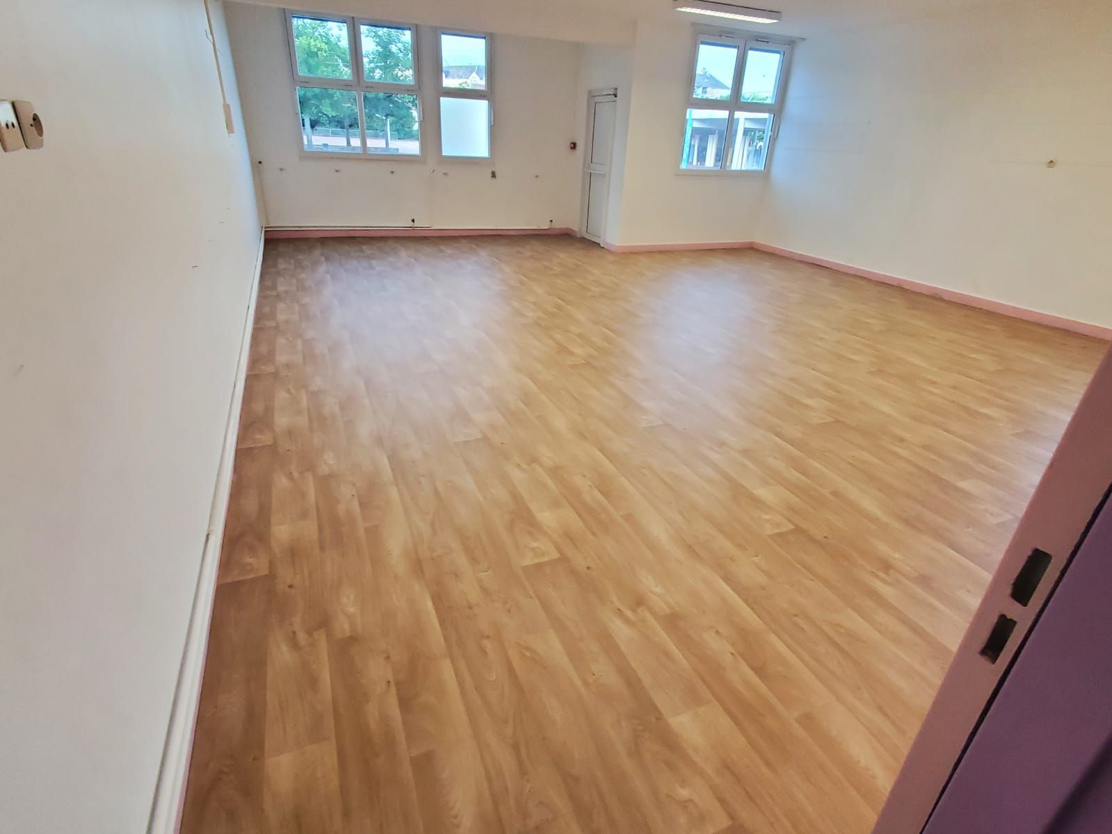 Pièce vide avec parquet clair, murs blancs et deux fenêtres laissant entrer la lumière du jour