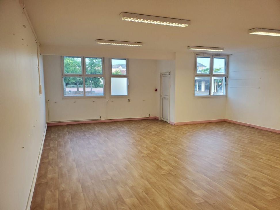 Pièce vide avec parquet, murs blancs et plusieurs fenêtres éclairées par des néons