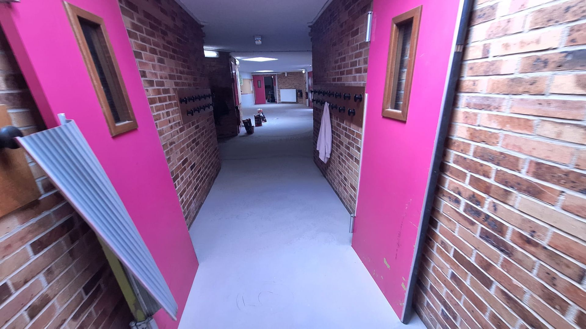 Couloir avec des encadrements de portes rose vif, des murs en briques et un sol blanc à l'intérieur d'un bâtiment