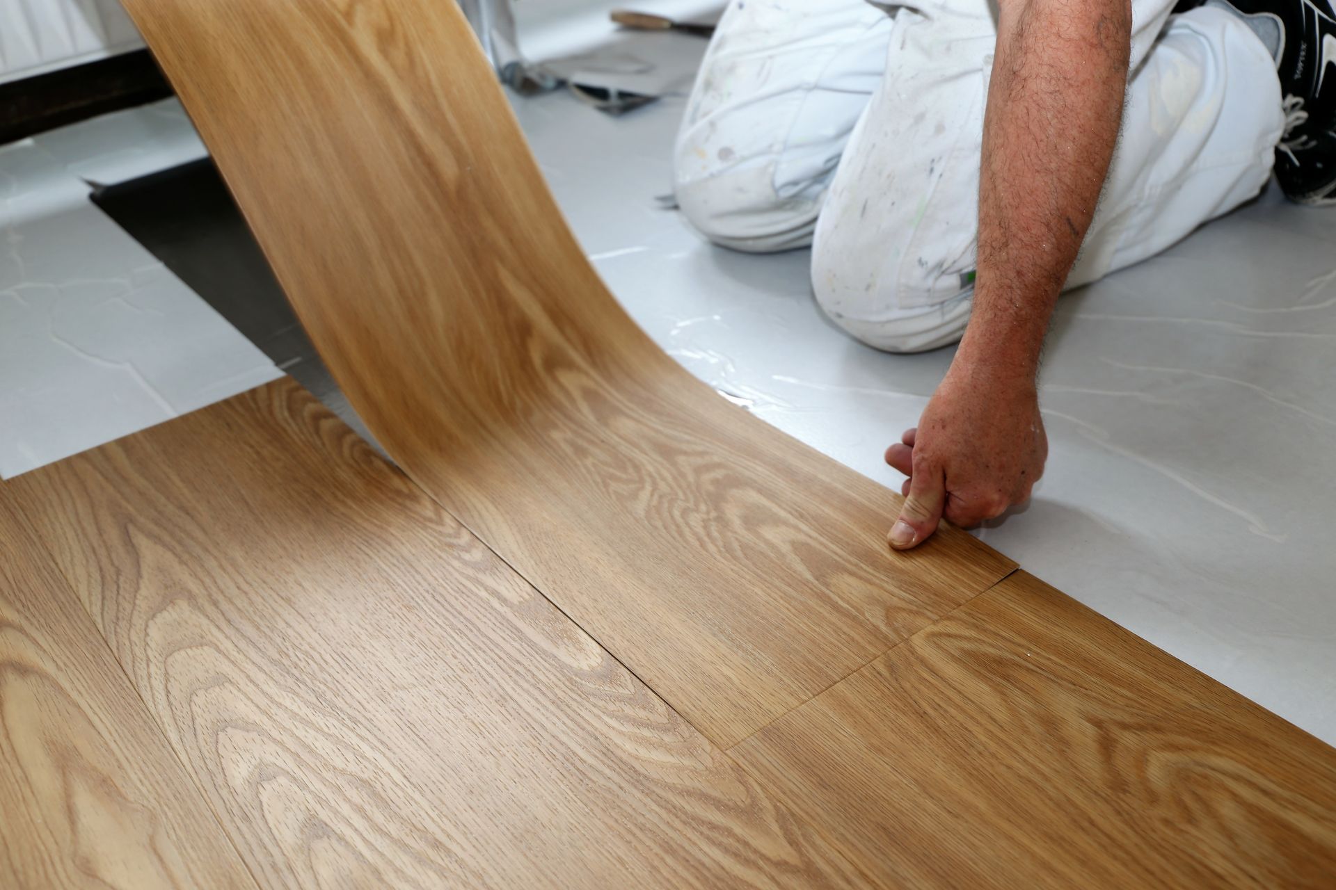 Pose de lames de parquet imitation bois sur un sol blanc, un ouvrier positionnant une lame.