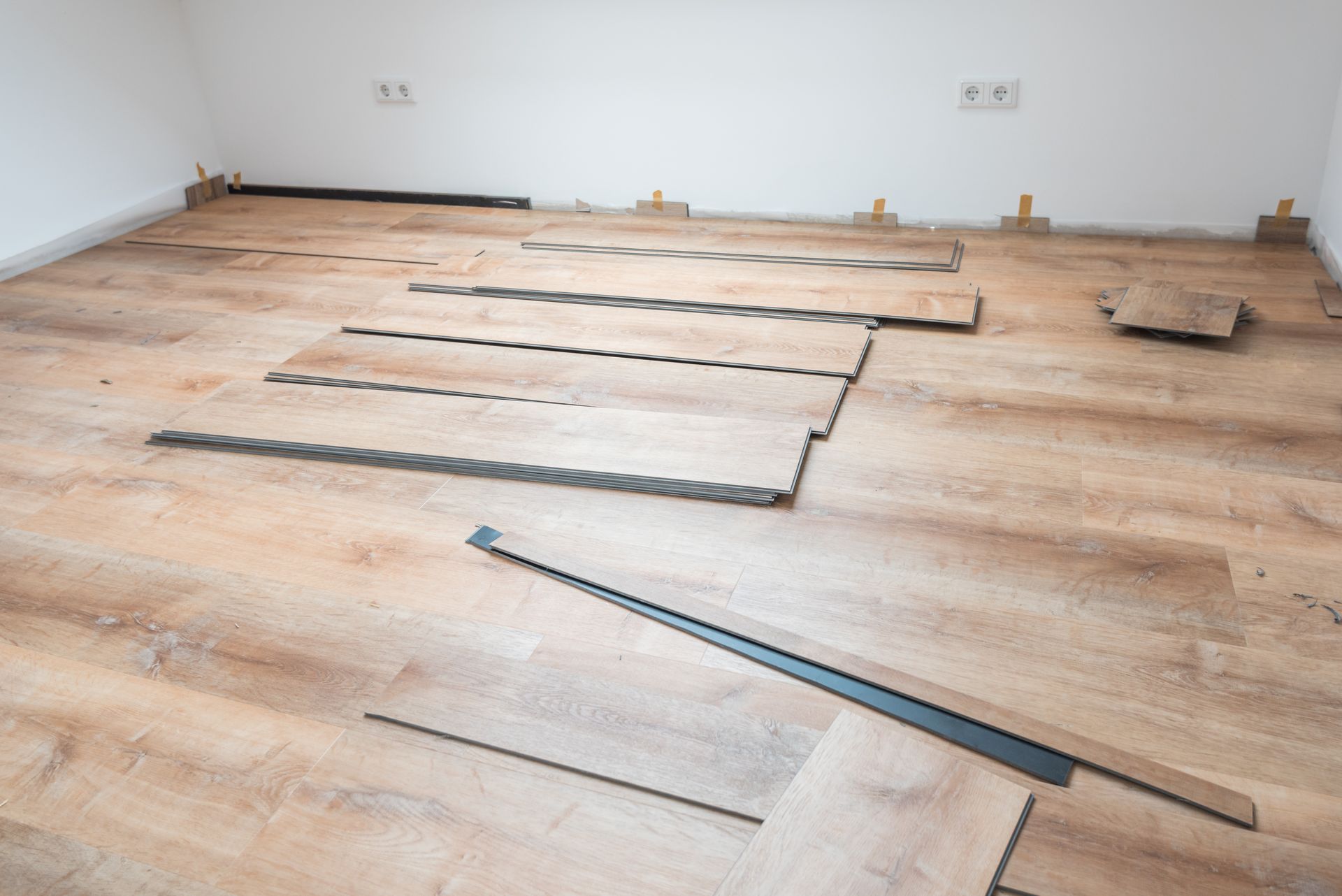 Parquet clair partiellement posé dans une pièce vide, lames non fixées et outils visibles.