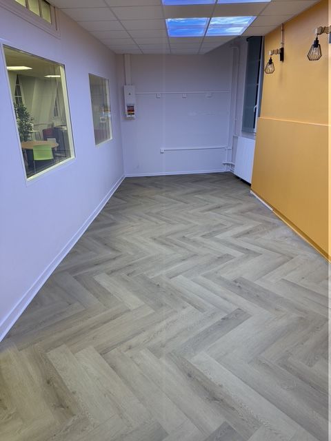 Couloir vide avec parquet à chevrons, murs blancs et un mur jaune à droite