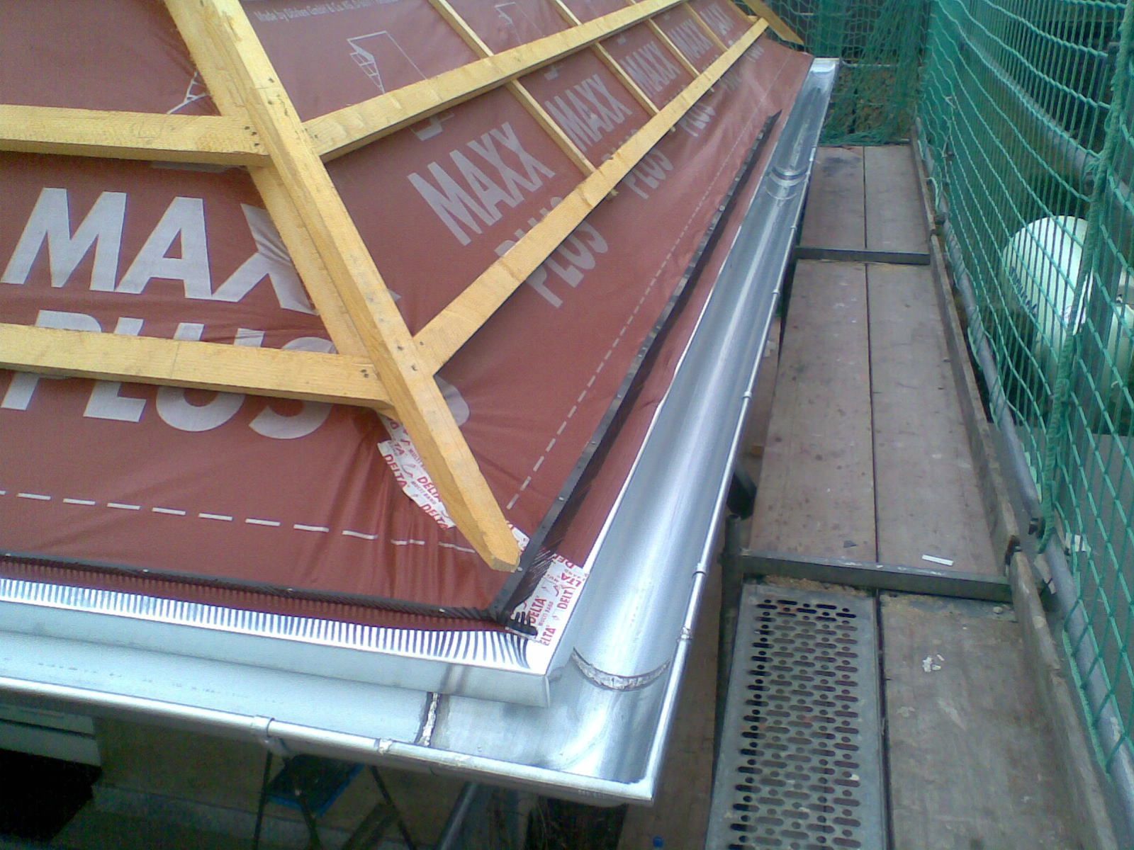 Ein im Bau befindliches Dach. Braune Unterspannbahn, Holzrahmen und eine Metallrinne.