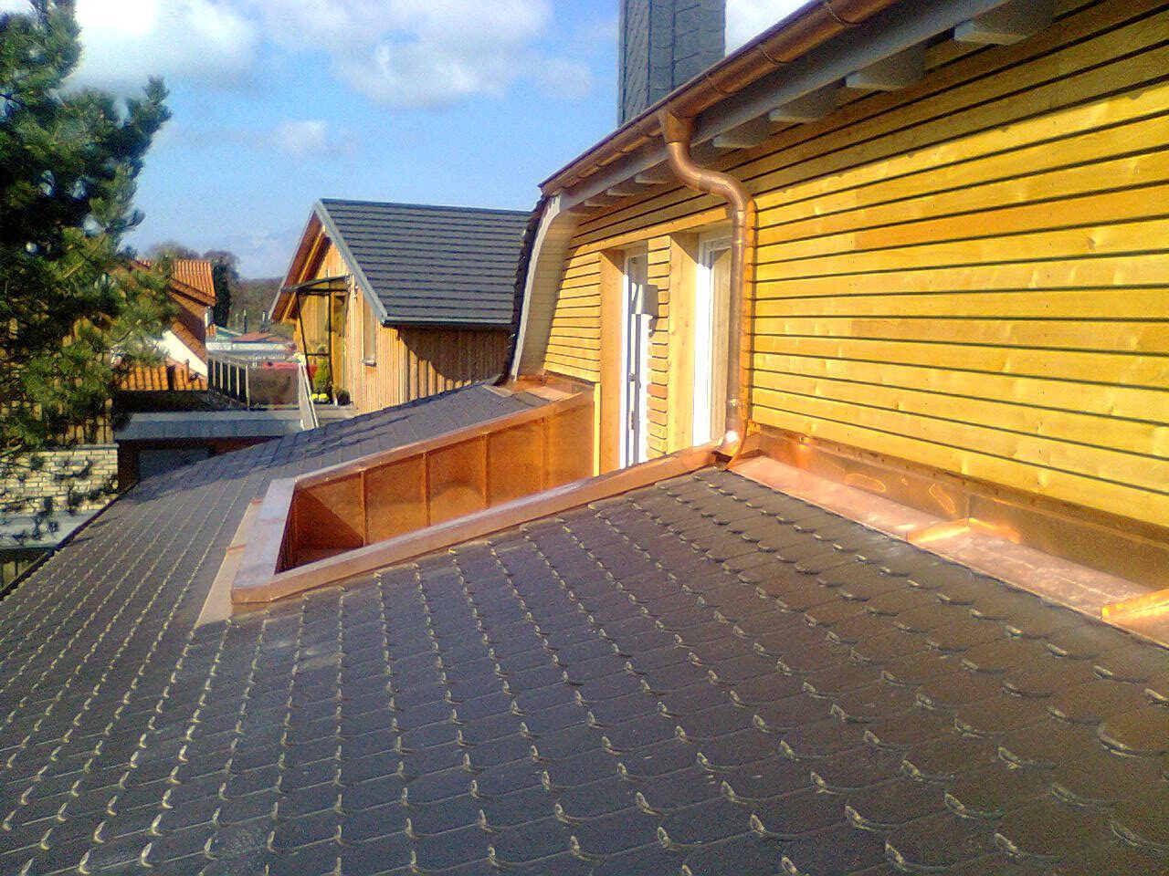 Kupferverziertes Dach mit dunklen Schindeln, eine Dachgaube und gelbe Holzverkleidung.