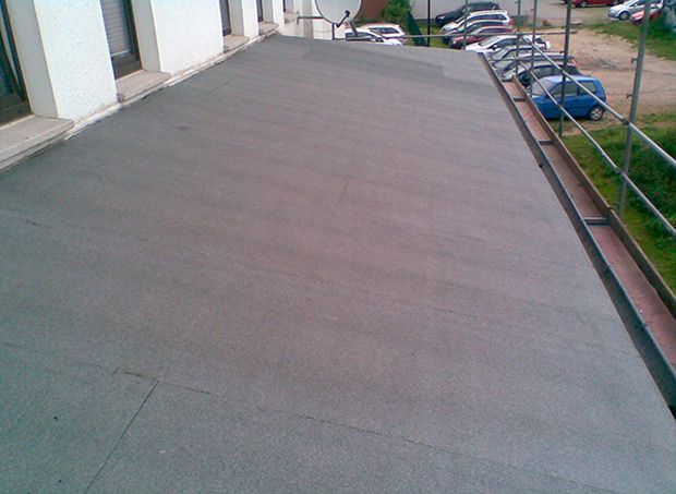 Flaches, graues Asphalt-Dach mit Metallgeländer und im Hintergrund geparkten Autos.