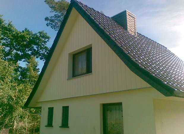 Ein Haus mit Satteldach, cremefarbener Fassade, dunklen Zierelementen und einem dunklen Ziegeldach.