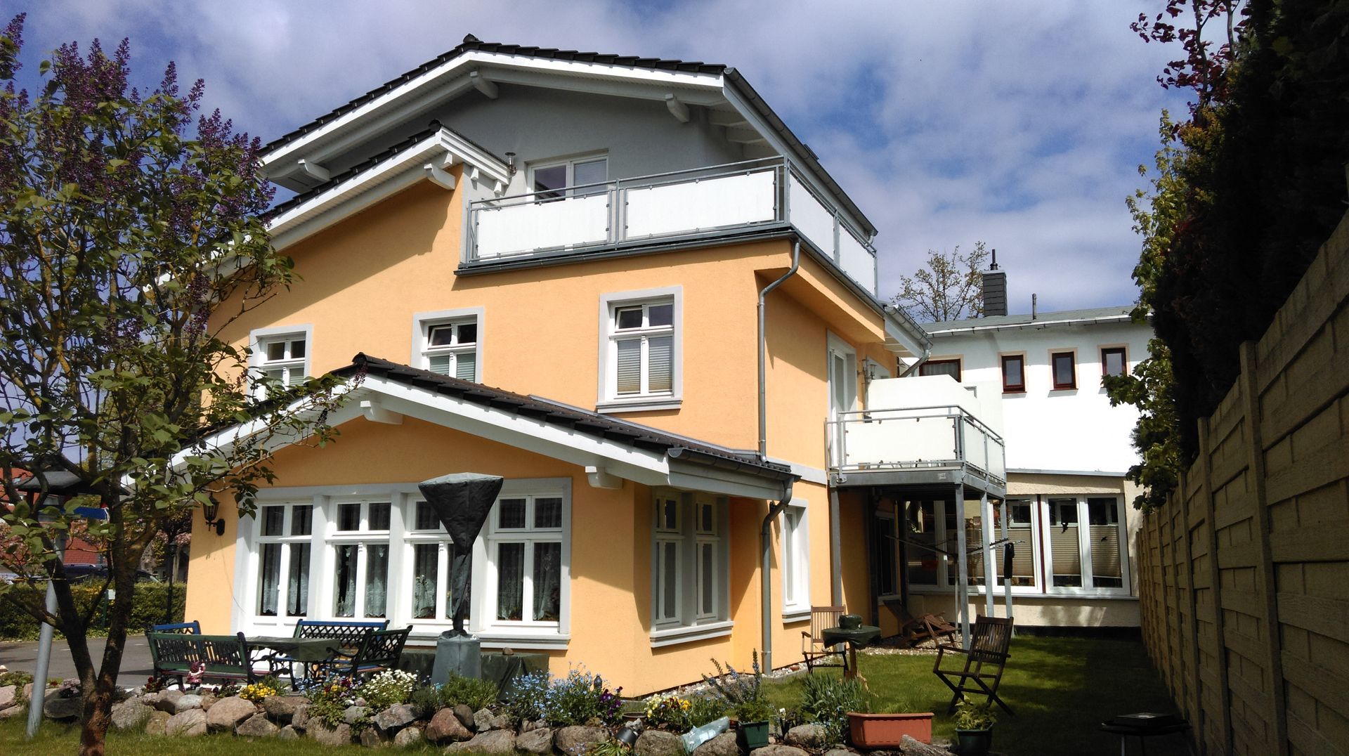 Gelbes Haus mit weißen Zierelementen und einem kleinen Vorgarten.