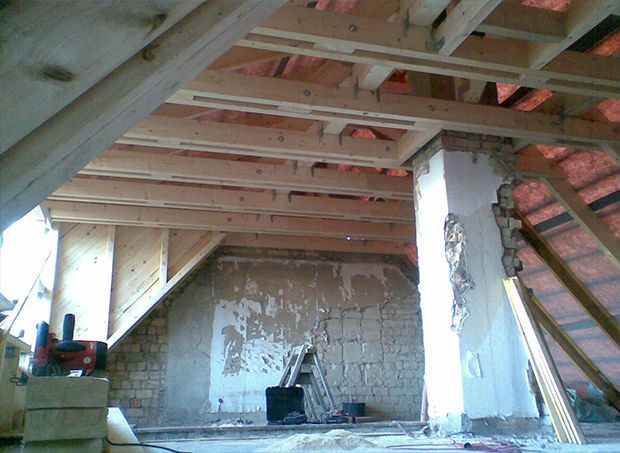 Innenansicht eines im Bau befindlichen Dachbodens mit freiliegenden Balken, teilweise abgerissenen Wänden und tragenden Konstruktionen.