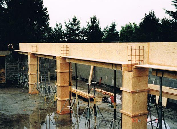 Baustelle: Holzschalungen für Säulen und Balken, Bewehrungsstahl sichtbar, Stützen angebracht, im Freien.