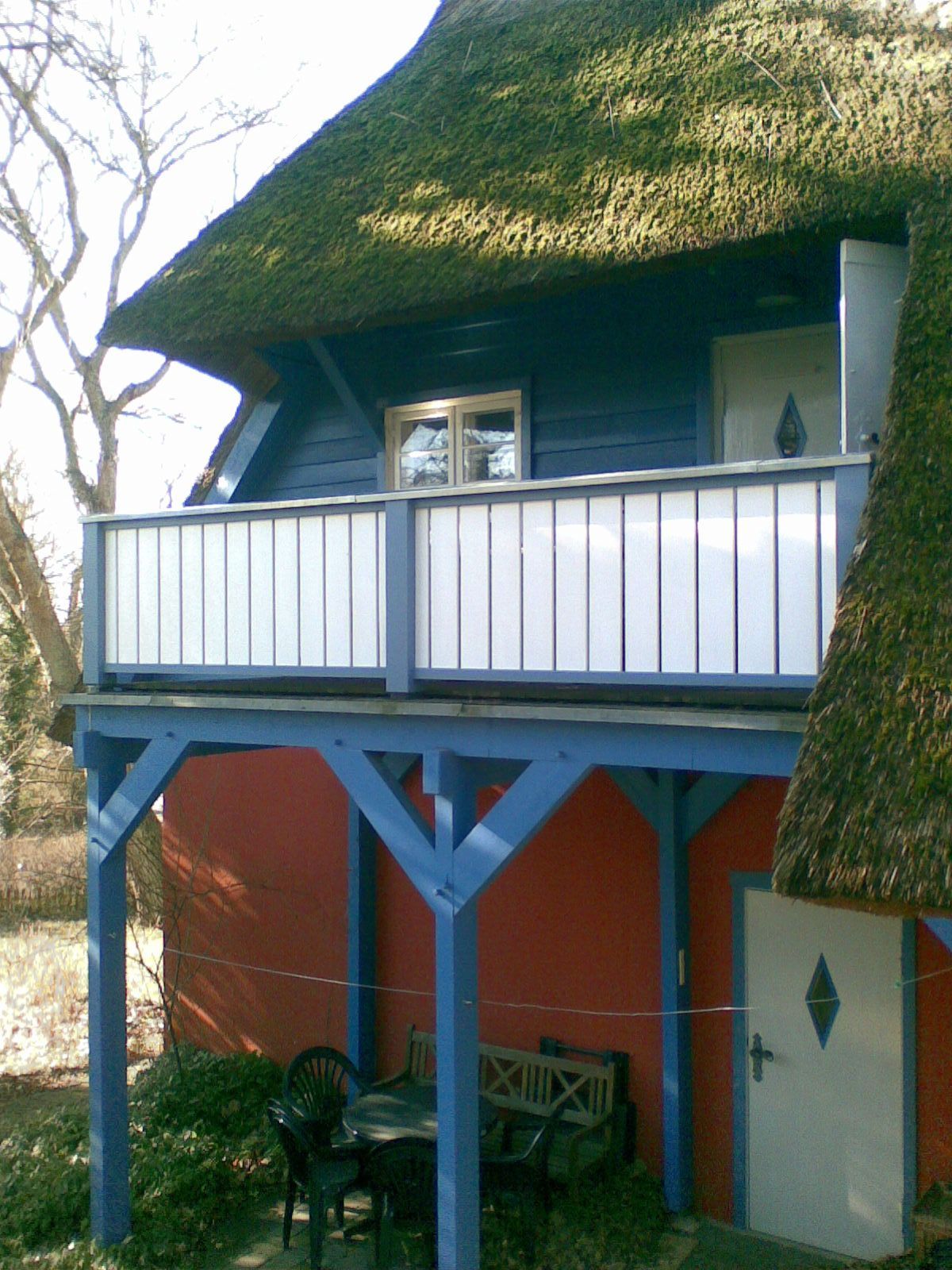 Blaues und rotes Häuschen mit Reetdach und Balkon.