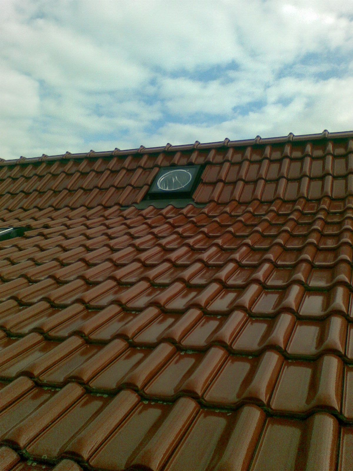 Rotes Ziegeldach mit Oberlicht vor bewölktem Himmel.