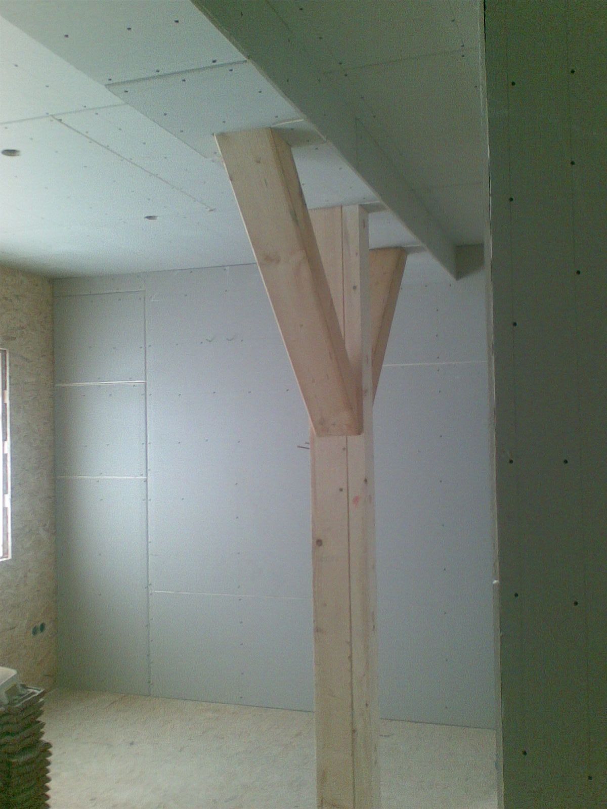 Eine hölzerne Stützsäule in einem im Bau befindlichen Raum, wobei die Decken- und Wandkonstruktion sichtbar ist.
