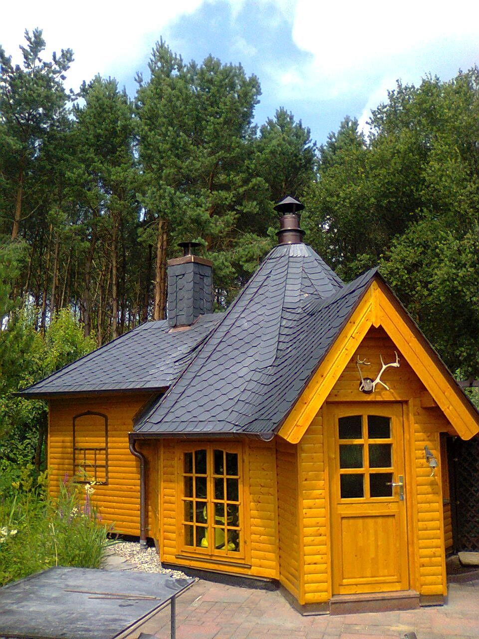 Gelbe Holzhütte mit dunkelgrauem Schindeldach und Schornstein, gelegen in einem Waldgebiet.