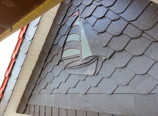 Dunkelgraues Schieferdach mit dreieckigem Fenster und geschichtetem Muster.