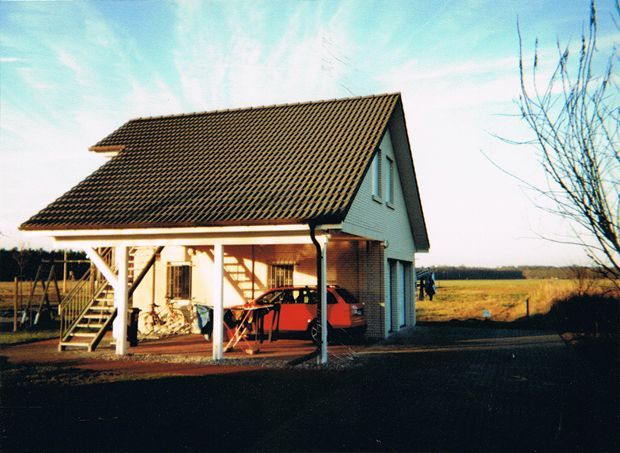 Garage mit Carport; rotes Auto unter dem Carport geparkt, helle Außenfarbe, braunes Dach und Treppe.