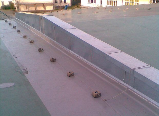 Eine Ansicht aus der Froschperspektive auf das Dach eines grauen Industriegebäudes mit einer langen, grauen rechteckigen Struktur und einer Reihe von Verankerungspunkten.