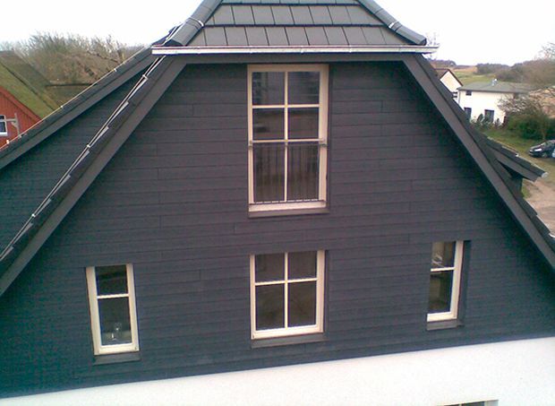 Dunkelgrauer Hausgiebel mit mehreren Fenstern und grauem Dach.