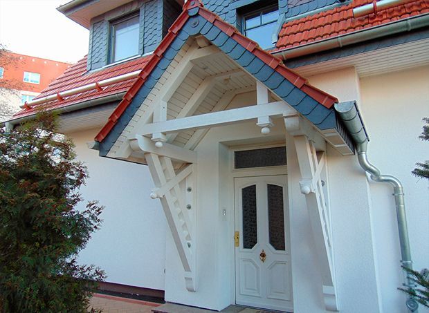 Weiße Eingangshalle mit Giebeldach aus Schiefer, rotem Ziegeldach und weißer Tür. Außenwand, Baum.