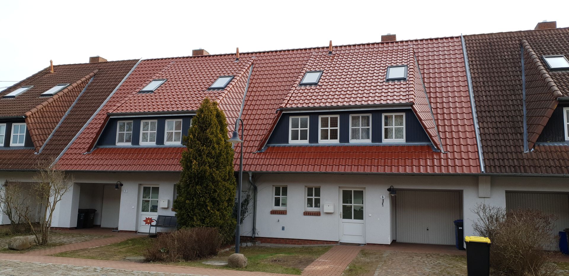 Eine Reihe von Stadthäusern mit roten Ziegeldächern und Dachgauben unter bedecktem Himmel.