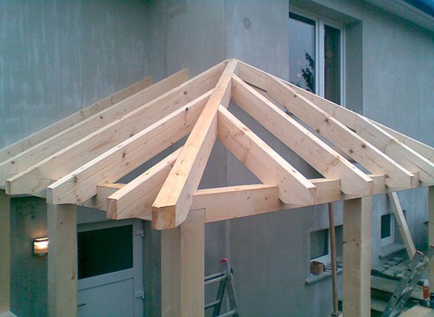 Im Bau befindliches hölzernes Verandadach, das an ein graues Gebäude angebaut ist.