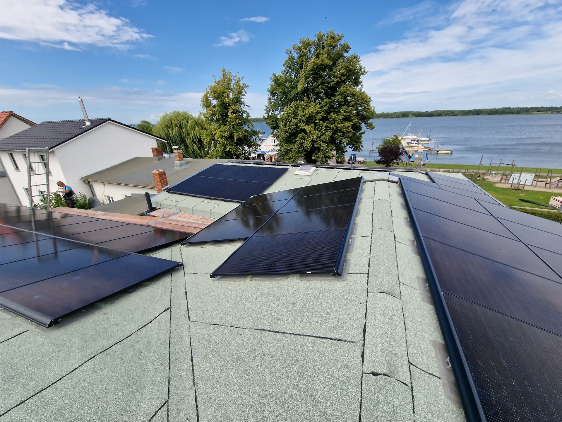 Auf einem Dach mit Blick auf einen See unter blauem Himmel wurden Solarpaneele installiert.