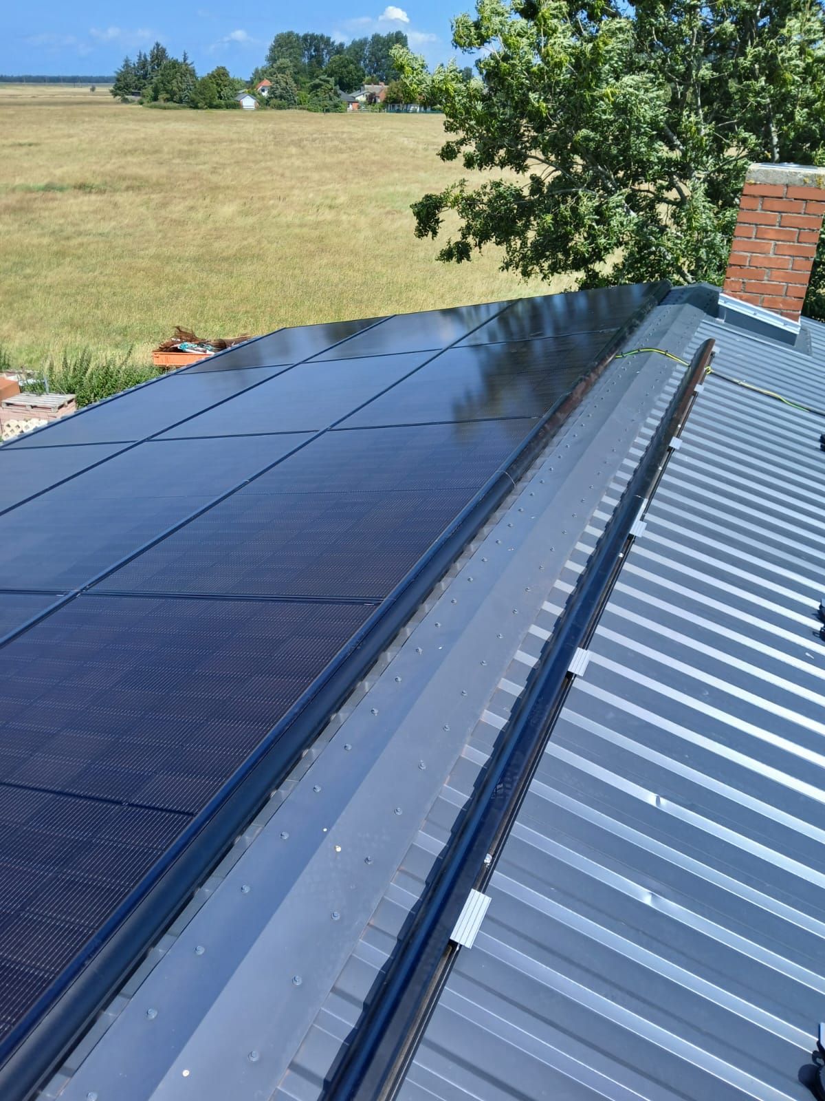 Solarpaneele auf einem Metalldach, im Hintergrund ein Schornstein und ein Feld.