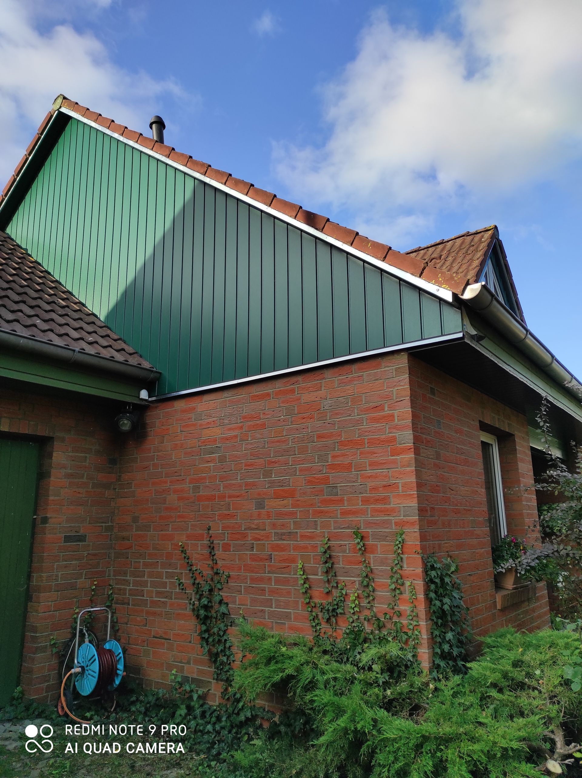 Backsteingebäude mit grüner Fassade, rotem Ziegeldach und blauem Himmel.