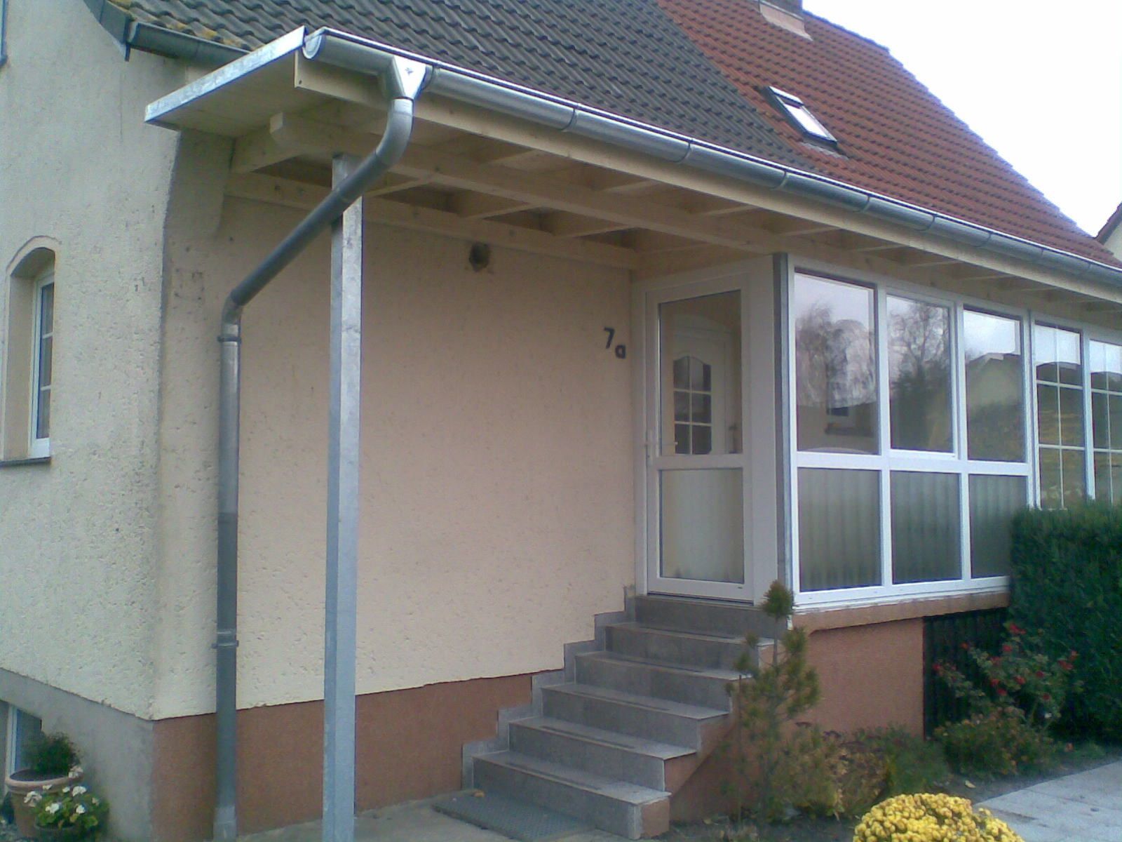 Beiges Haus mit Veranda, Treppe und Glasfenstern. Silberne Dachrinne und Fallrohr.