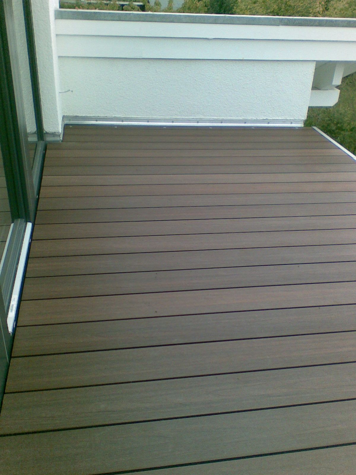 Braune Verbundholzterrasse auf einem Balkon mit weißer Wand.