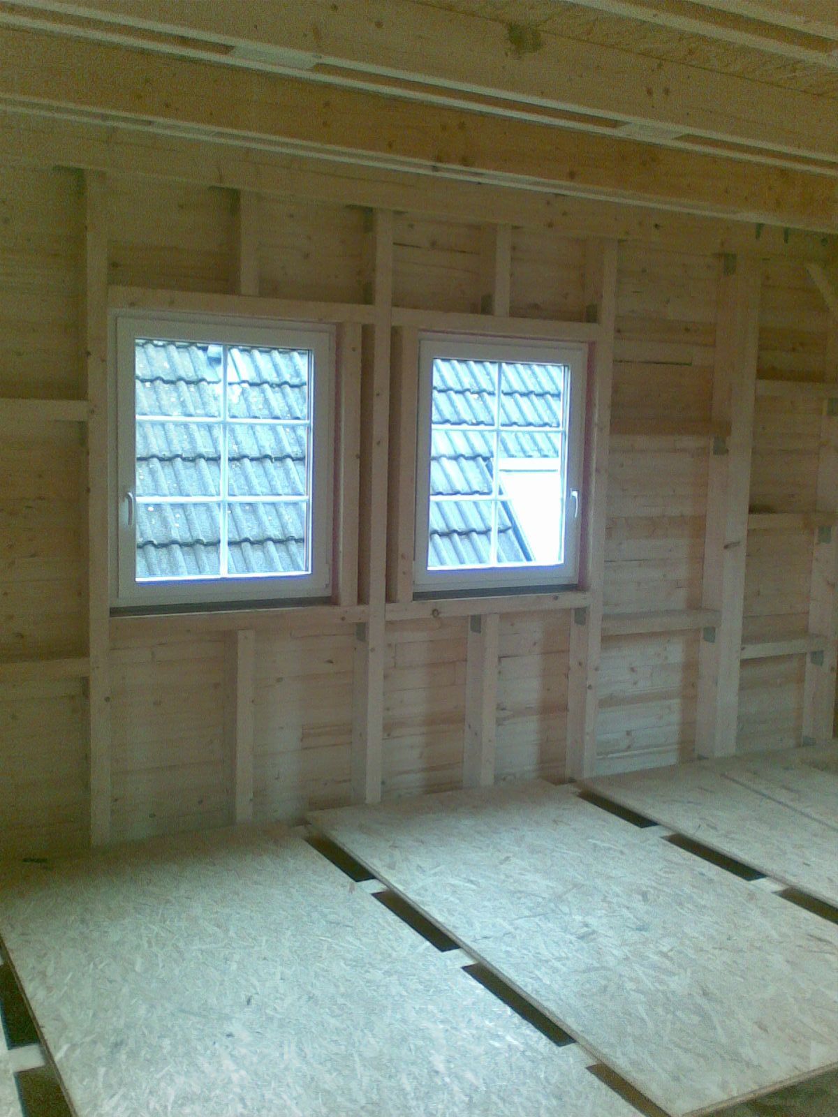 Innenansicht eines im Bau befindlichen Gebäudes mit gerahmten Fenstern, Holzvertäfelung und Spanplattenboden.