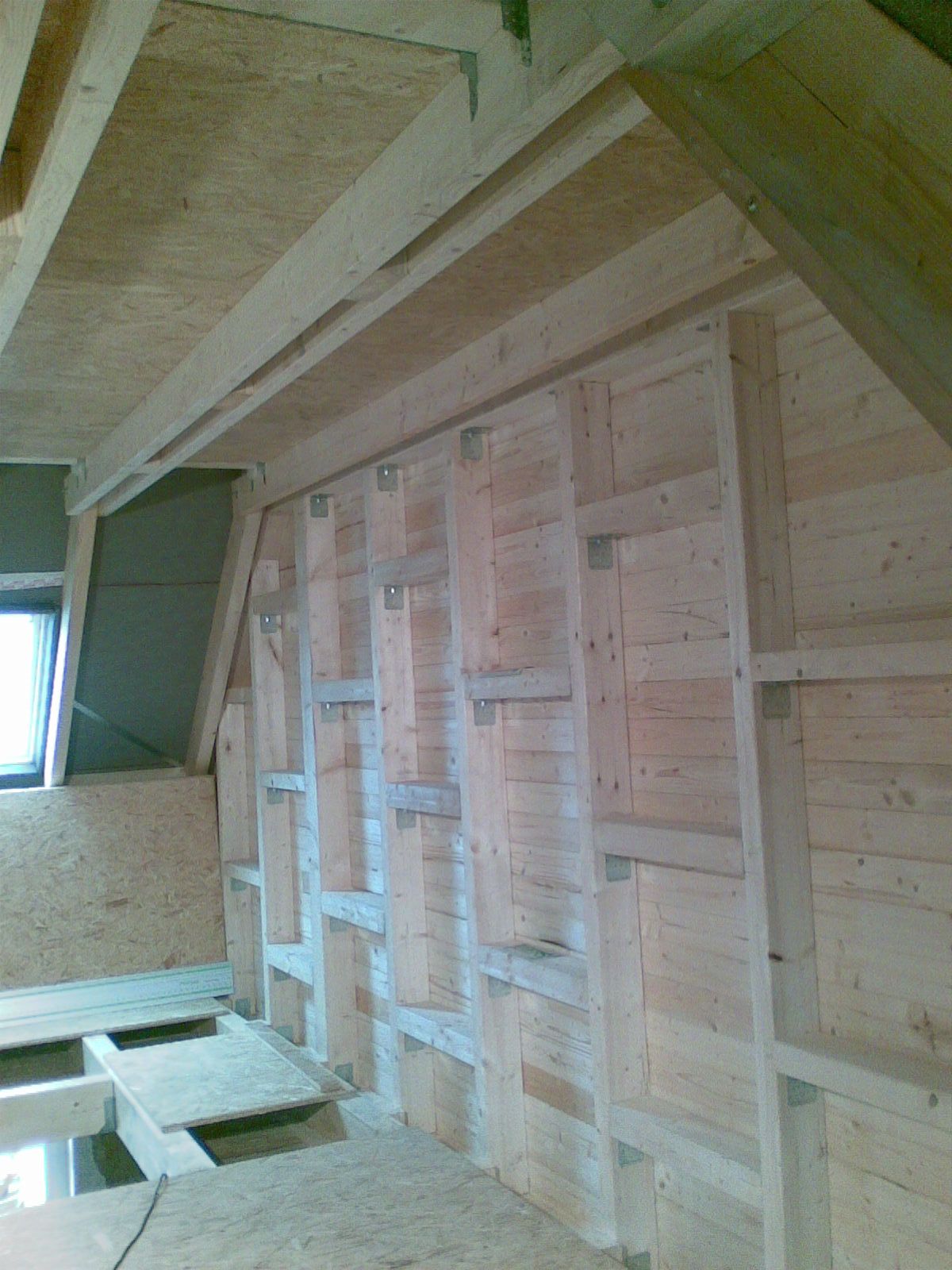 Innenansicht eines im Bau befindlichen Raumes mit freiliegendem Holzfachwerk und tragenden Konstruktionselementen.