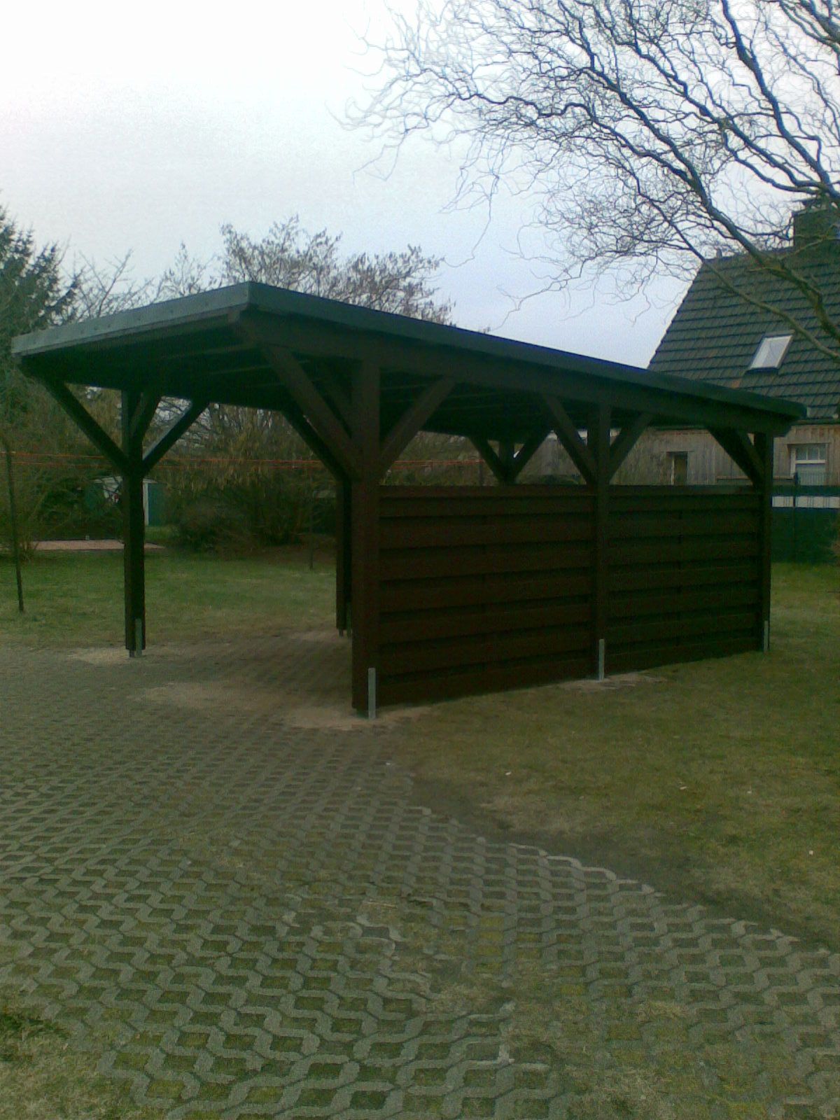 Holzcarport mit braunem Dach und brauner Verkleidung auf einem grünen Rasen.