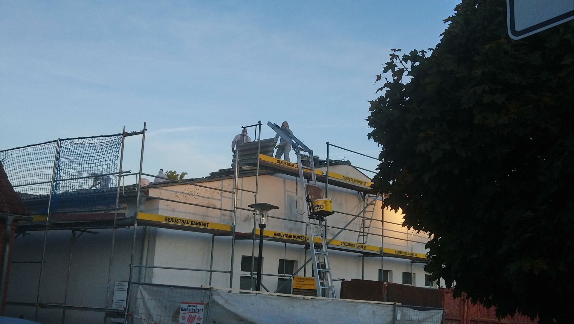 Gebäude im Bau; ein Gerüst umgibt ein weißes Gebäude, Arbeiter auf dem Dach, Sicherheitsnetze.