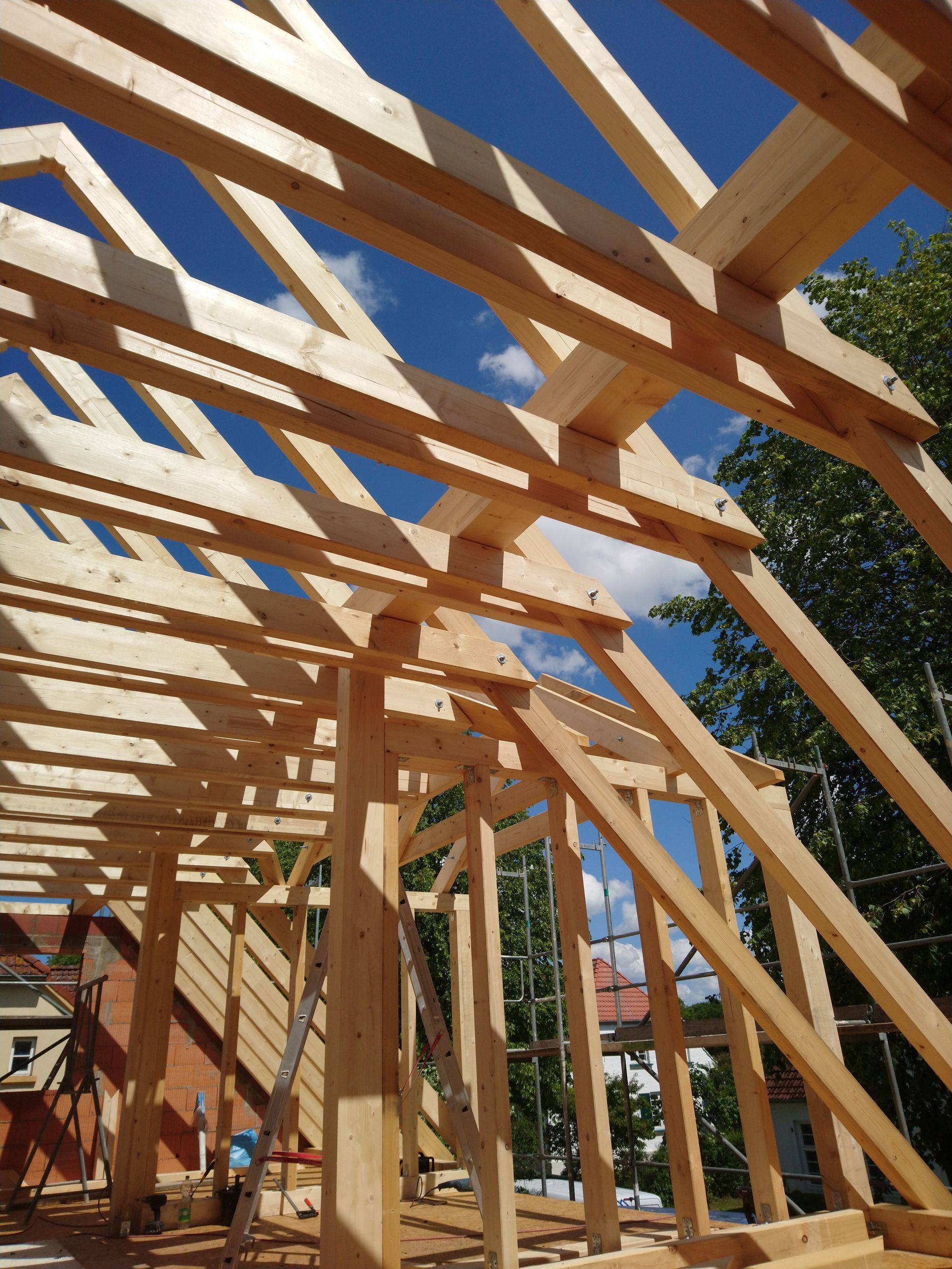 Im Bau befindliche hölzerne Dachkonstruktion vor strahlend blauem Himmel.