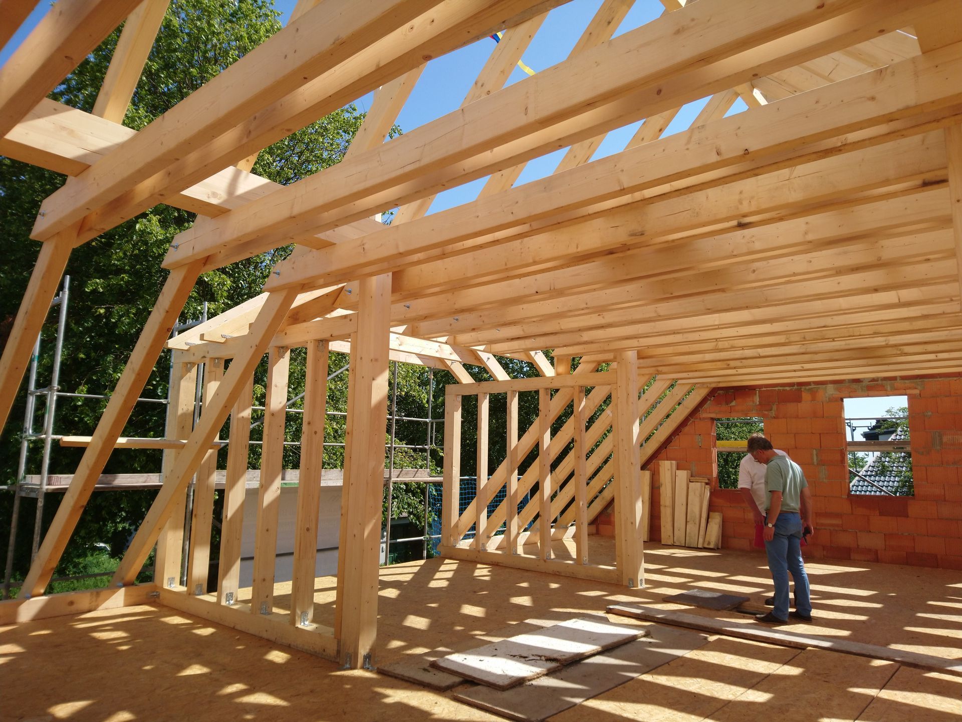 Innenansicht eines Hauses in Holzrahmenbauweise. Eine Person arbeitet auf dem Boden in der Nähe eines offenen Fensters. Sonnenlicht strömt herein.