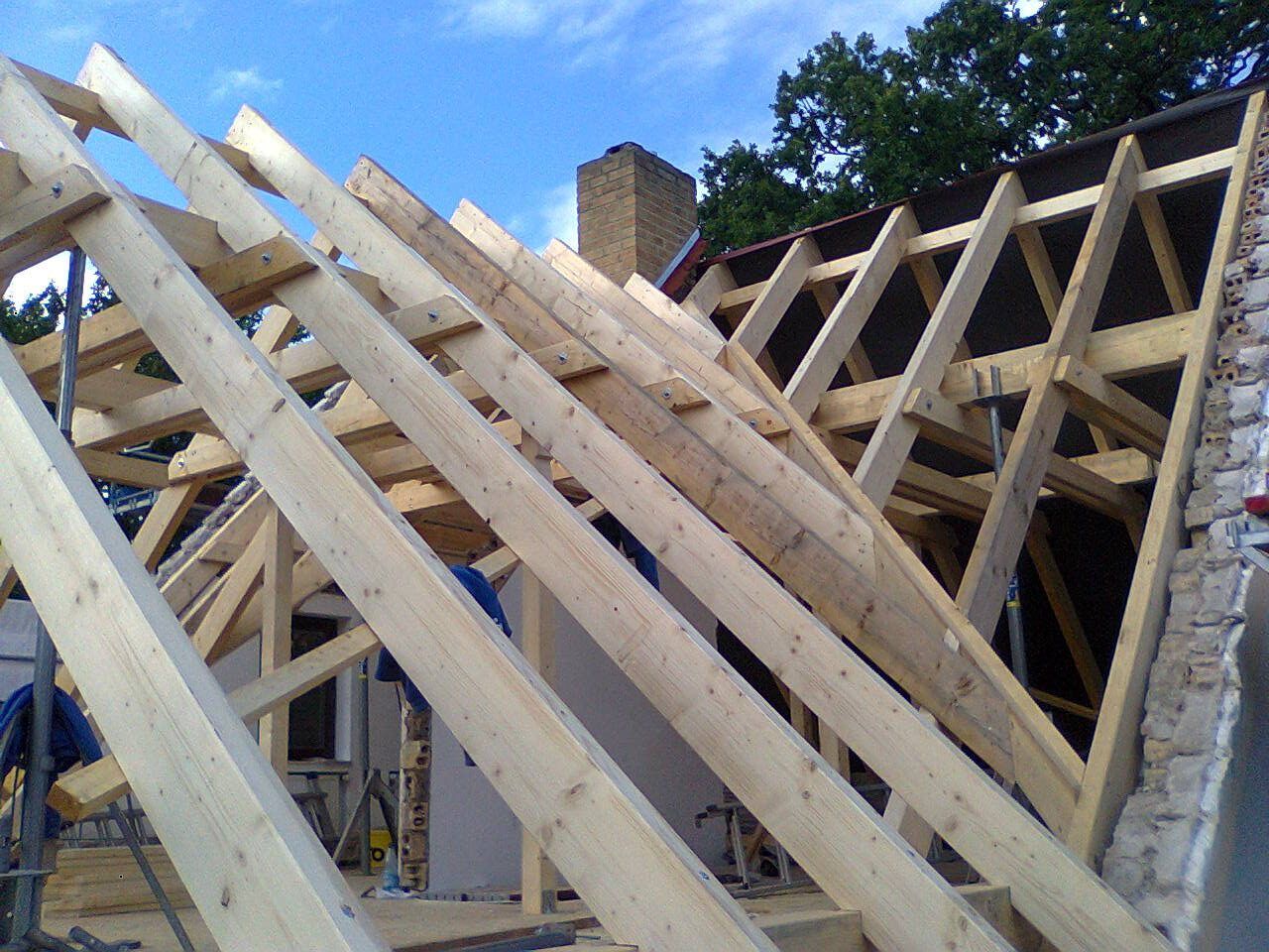 Im Bau befindliche hölzerne Dachsparren mit einem Schornstein und blauem Himmel im Hintergrund.