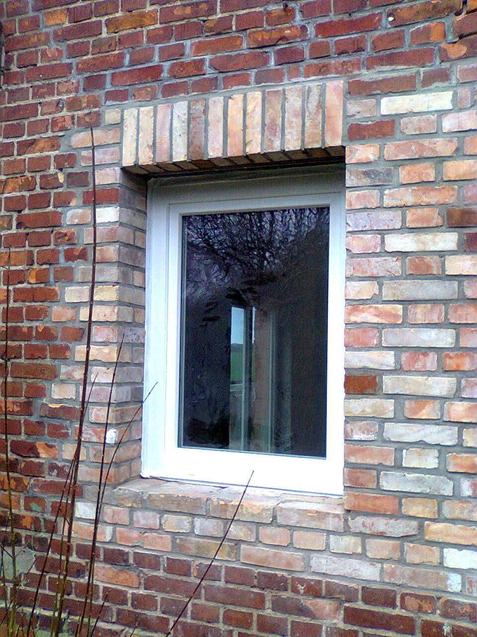 Ein weiß gerahmtes Fenster in einer Backsteinmauer. Hellere Ziegel umgeben das Fenster, dunklere Ziegel bilden den Rest der Fassade.