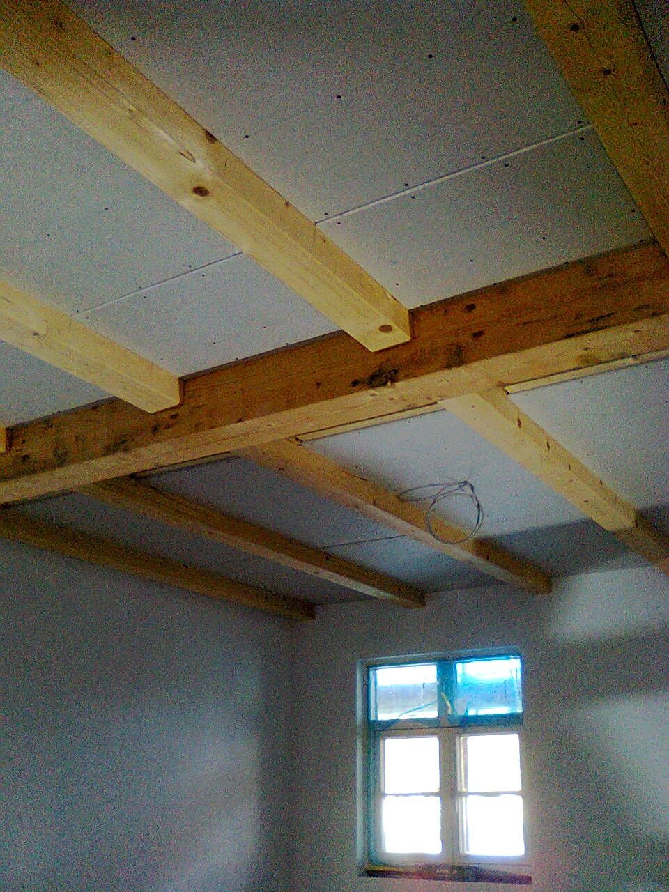 Innenansicht eines Zimmers mit einer Decke aus Holzbalken und einem Fenster.