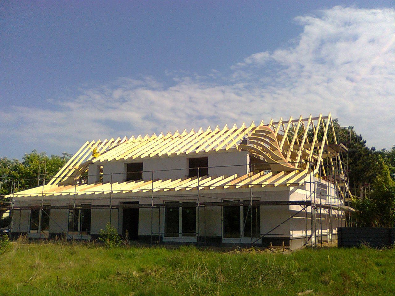 Haus im Bau; hölzernes Dachgerüst, weiße Wände, Gerüst, strahlend sonniger Tag.