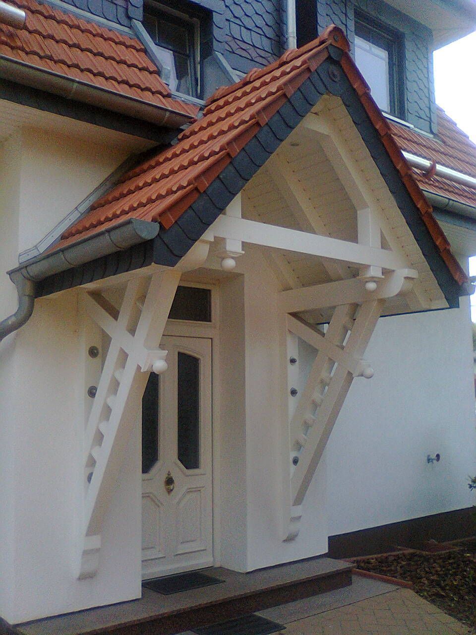 Weißes Holzvordach über der Eingangstür eines weißen Hauses mit roten Dachziegeln.