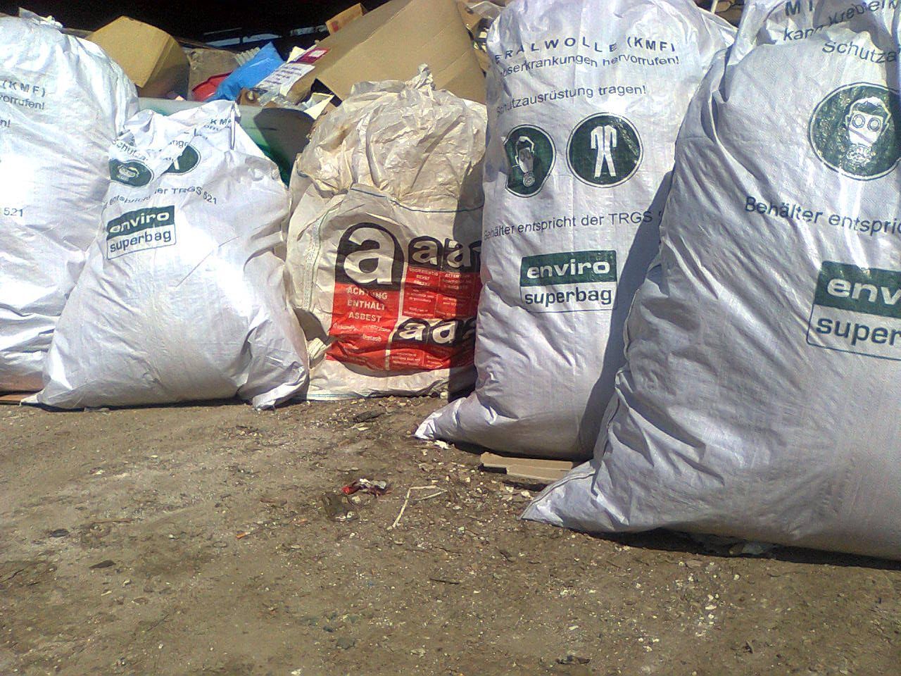 Müllsäcke und Wertstoffsäcke auf einer Betonfläche, einige mit grünem „Umwelt“-Logo.