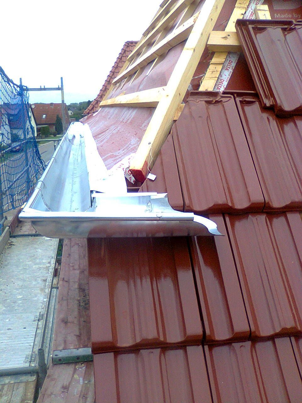 Installation eines Daches mit roten Ziegeln und einer Metalleinfassung am Rand.