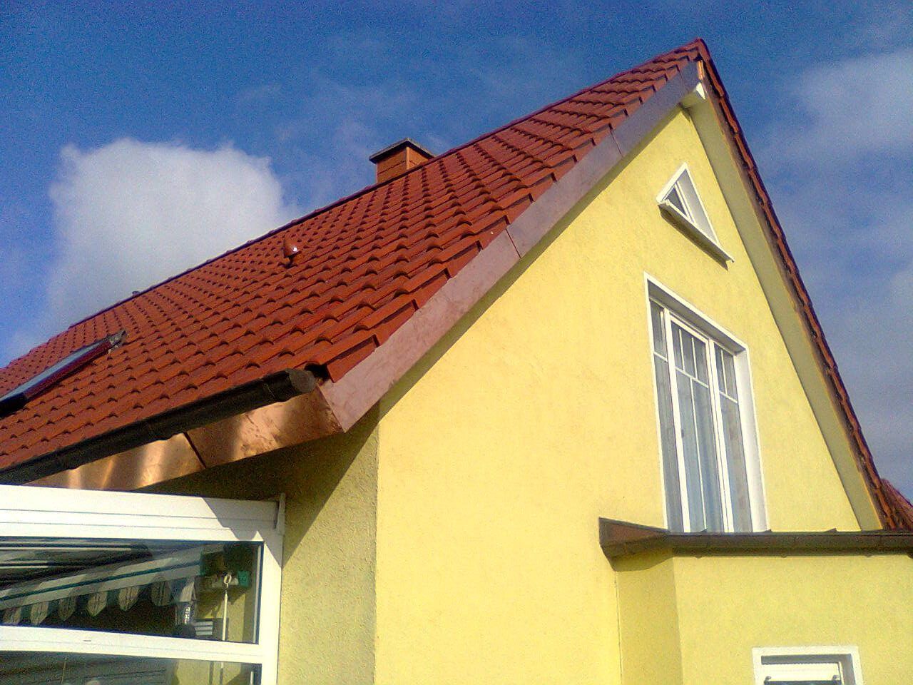 Gelbes Haus mit rotem Ziegeldach, weißen Fenstern und Zierleisten, blauer Himmel.