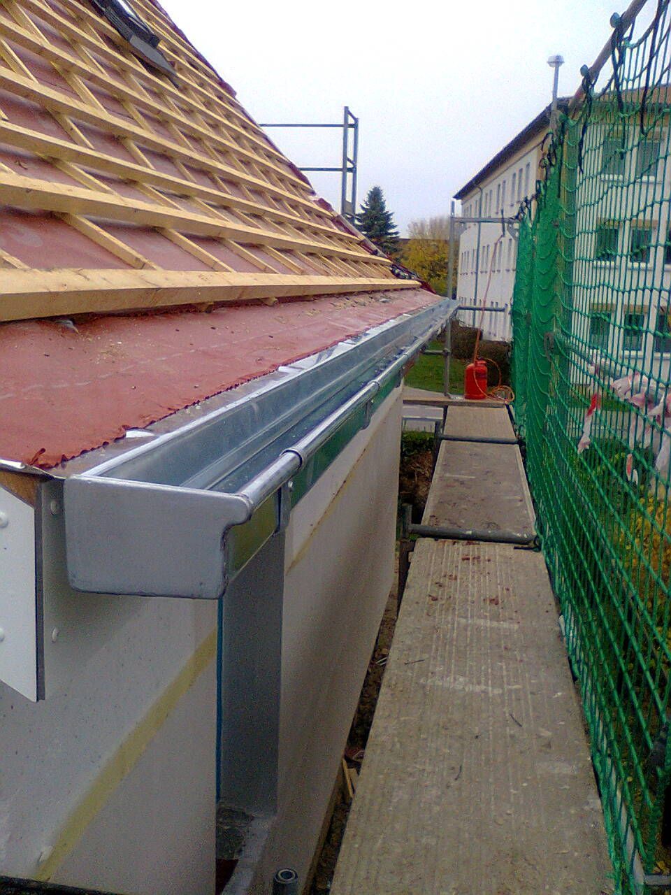 Neue Metallrinne auf einem im Bau befindlichen Dach installiert; Sicherheitsnetz und Gerüst vorhanden.