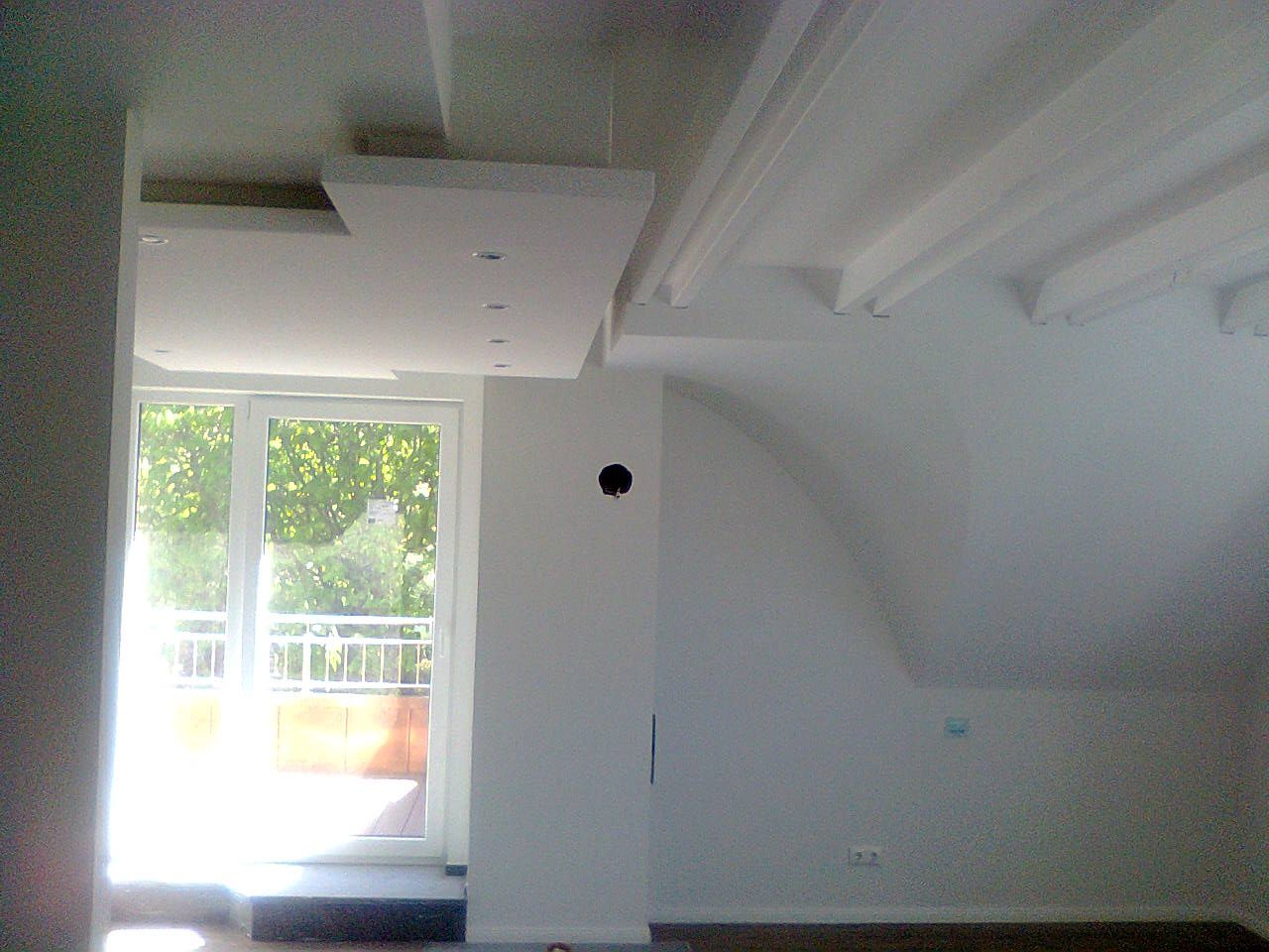 Innenansicht eines weißen Zimmers mit Balkontür, Dachschräge und rechteckigem Deckenelement.