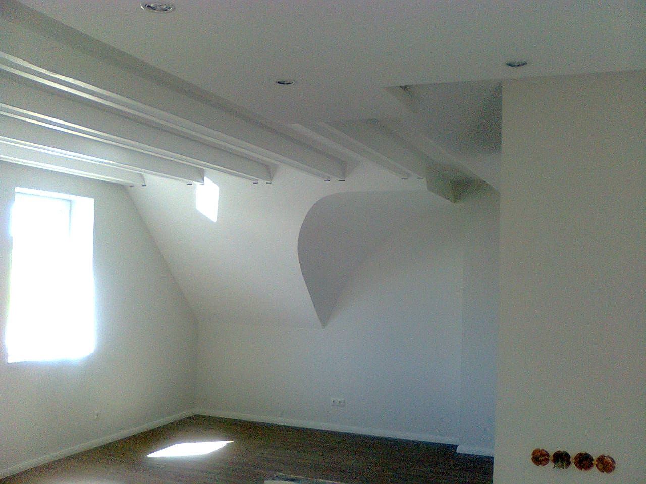 Ein leerer, weißer Raum mit Dachschräge und Fenster. Neonlicht und Holzboden.