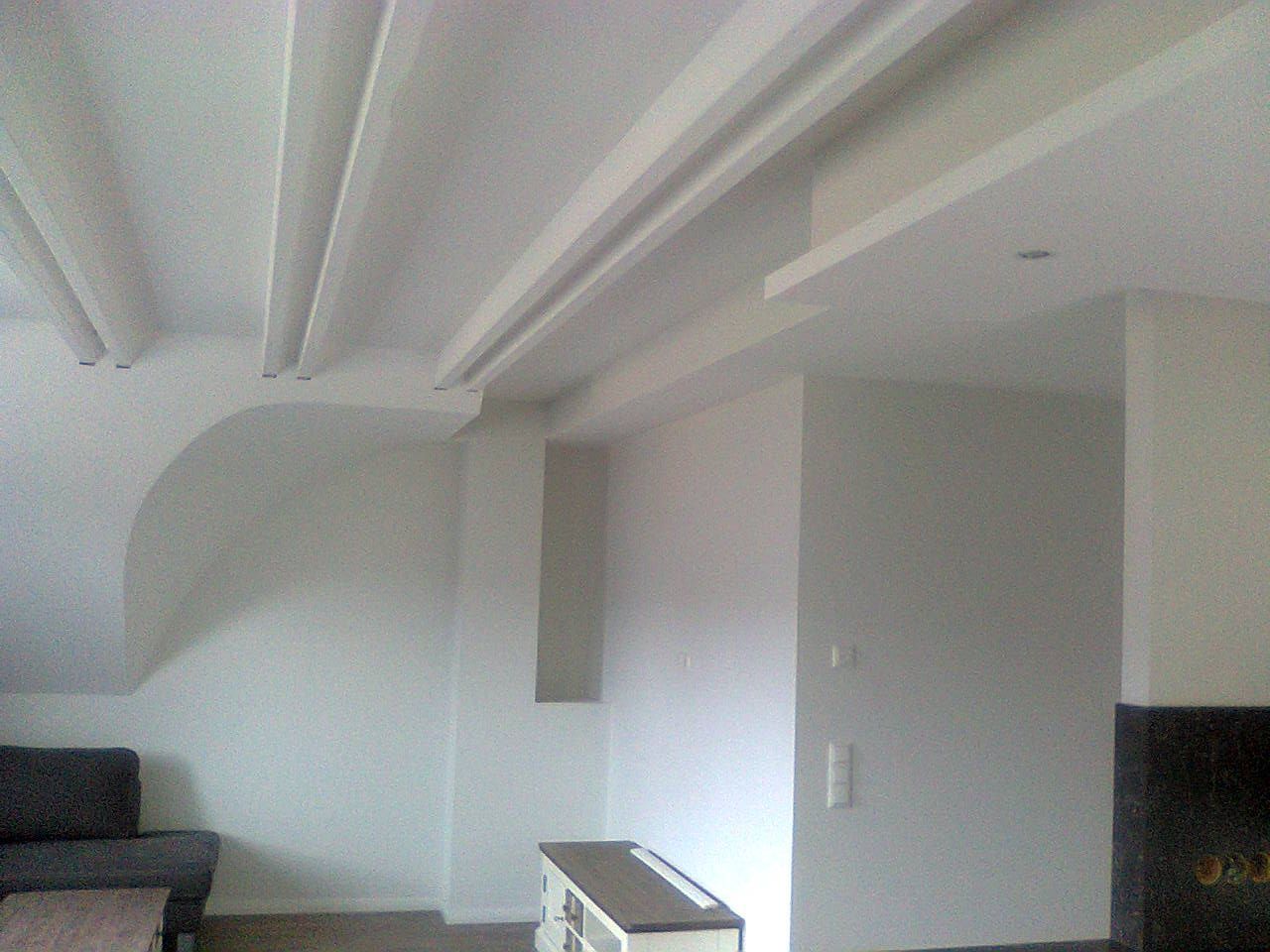 Weiß getünchtes Zimmer mit Sofa, Schrank und einer Decke mit Balken und Zierleisten.